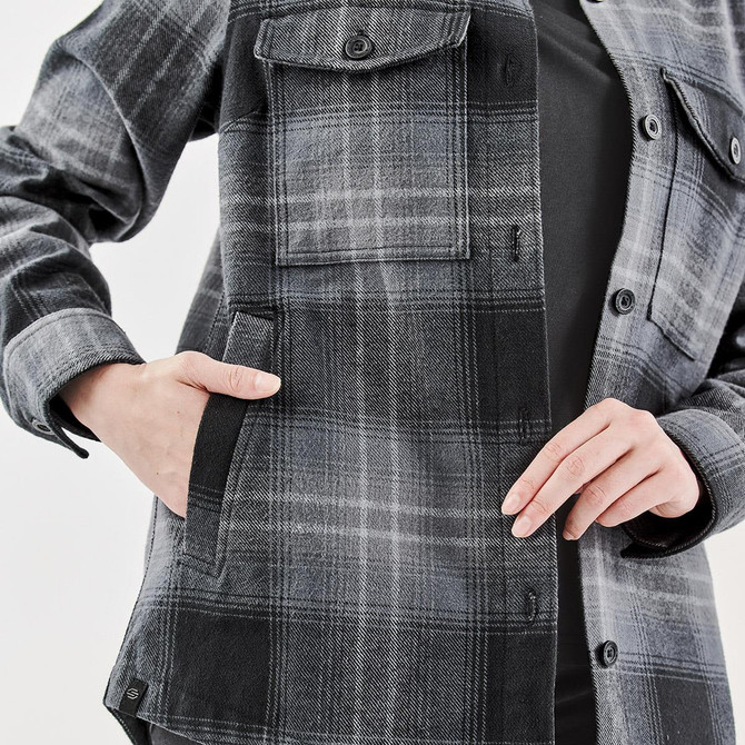 A women's shacket in grey and black Highland plaid with a front pocket and button closure. Features a logo.