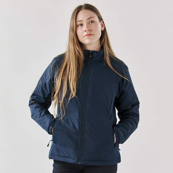 A woman wearing a navy blue thermal jacket with a zippered front and side pockets, featuring a logo.