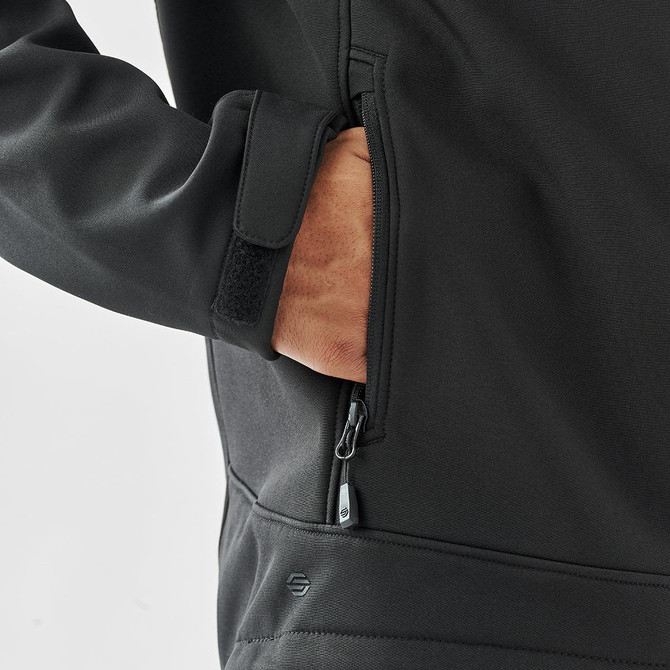 A black softshell jacket with a zippered pocket, featuring a hand reaching inside the pocket.