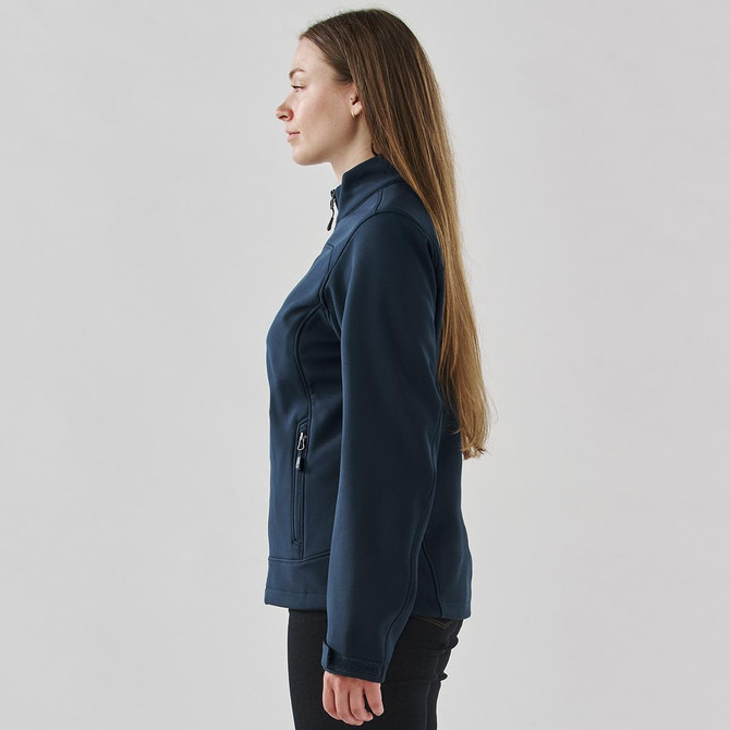 A softshell jacket in navy blue, featuring a zip pocket, shown from the side on a model with long hair.