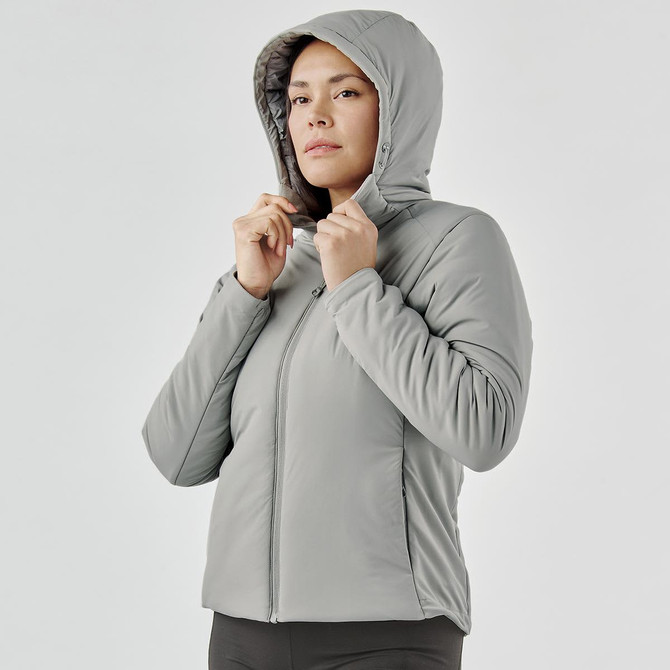A woman is wearing a grey puffer jacket with a hood, featuring a zip-up front and a fitted silhouette.