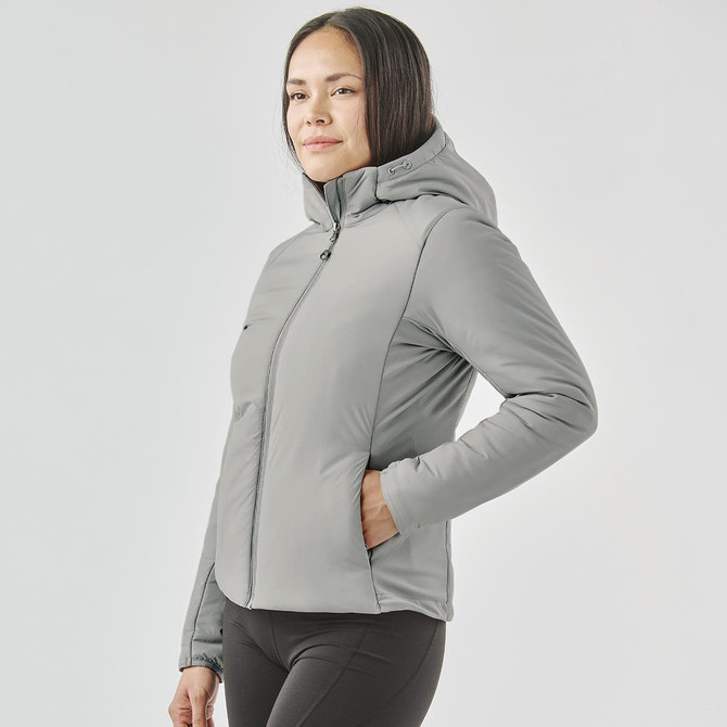 A woman wearing a grey thermal puffer jacket with a hood, featuring side pockets and a fitted design.