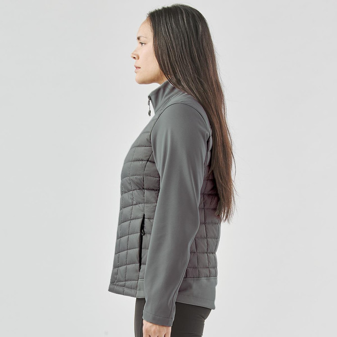 A woman stands sideways wearing a grey Women's Appalachian Thermal Softshell Jacket. The jacket features a quilted design and a logo.