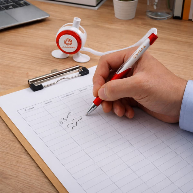 A red and white pen is being used to write on a clipboard with a blank page on a wooden desk.