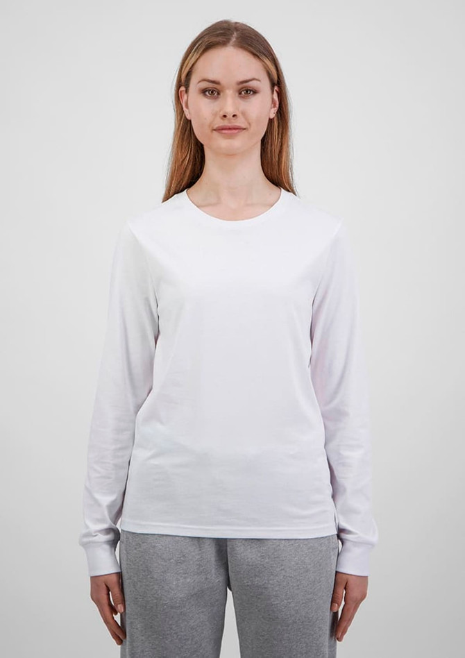 A woman wears a white long sleeve tee, paired with grey trousers. The tee features a simple design and has a logo.