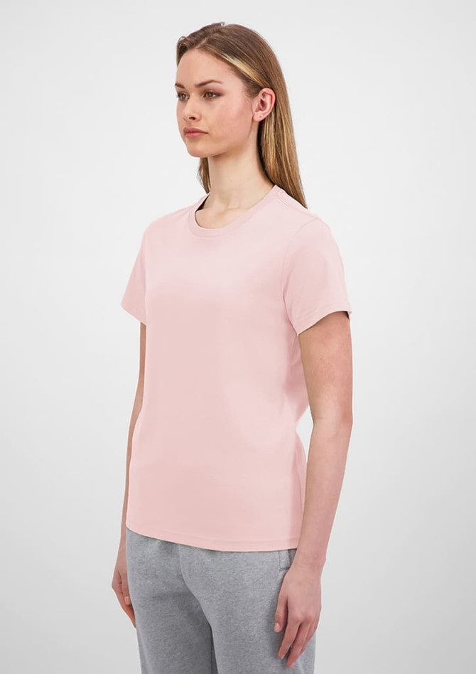 A light pink women's short sleeve tee displayed on a model with straight hair, paired with grey bottoms.