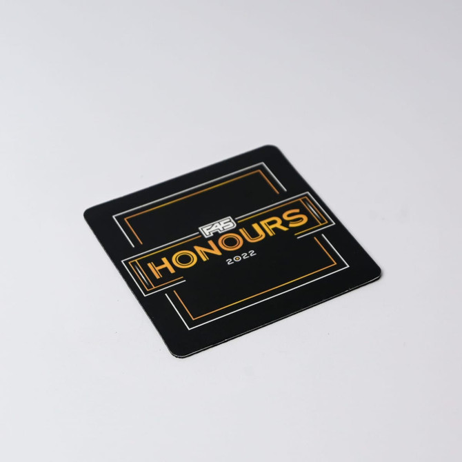 A square black coaster featuring a gold and white logo and the word "HONOURS" with the year "2022".