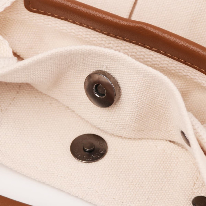 A close-up of a beige canvas tote bag interior, featuring brown leather accents and metal snap fasteners.