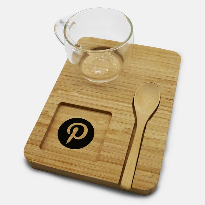 A glass cup, bamboo tray, and wooden spoon, featuring a logo on the tray. Natural tones dominate the set.