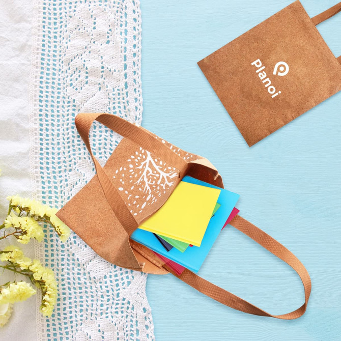 A cork tote bag in brown with a design, containing colourful sticky notes, placed on a light blue surface.