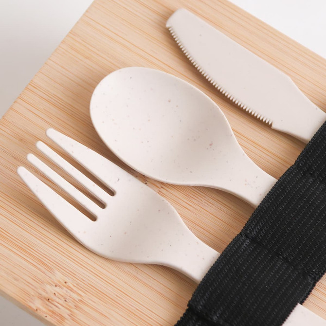 A bamboo-covered lunch box with light-coloured utensils laid on top, secured with a black strap.