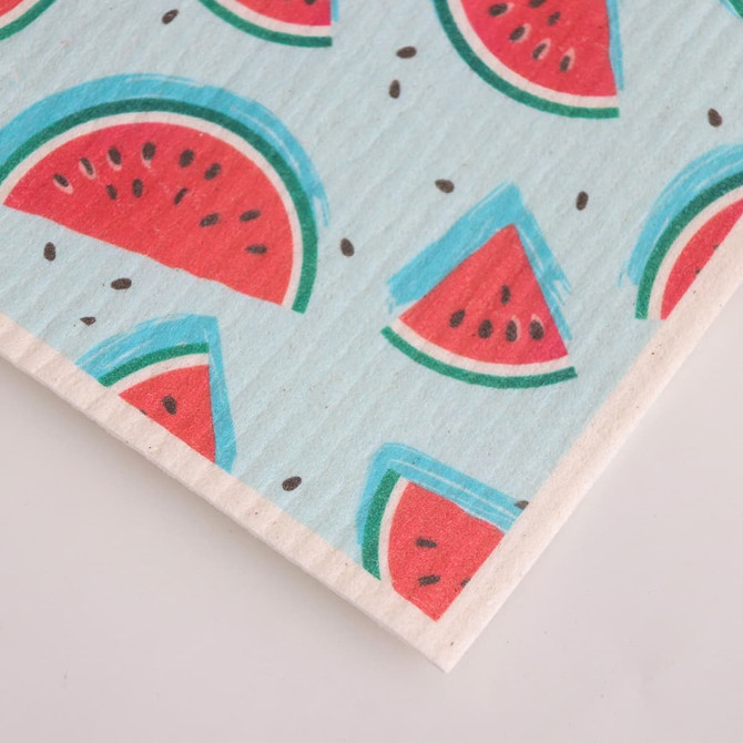 A biodegradable dishwashing cloth featuring a light blue background with red watermelon slice patterns and black seeds.