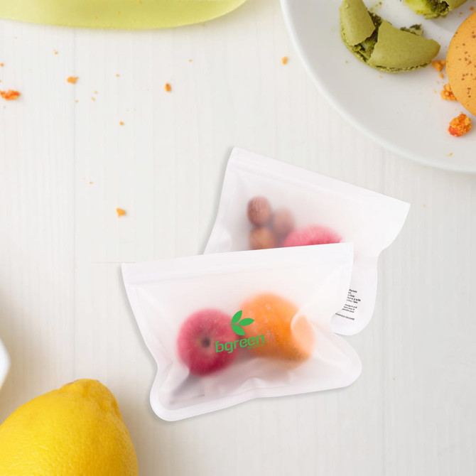 Two small transparent storage bags containing various colourful fruits, placed on a light wooden surface with some food items nearby.