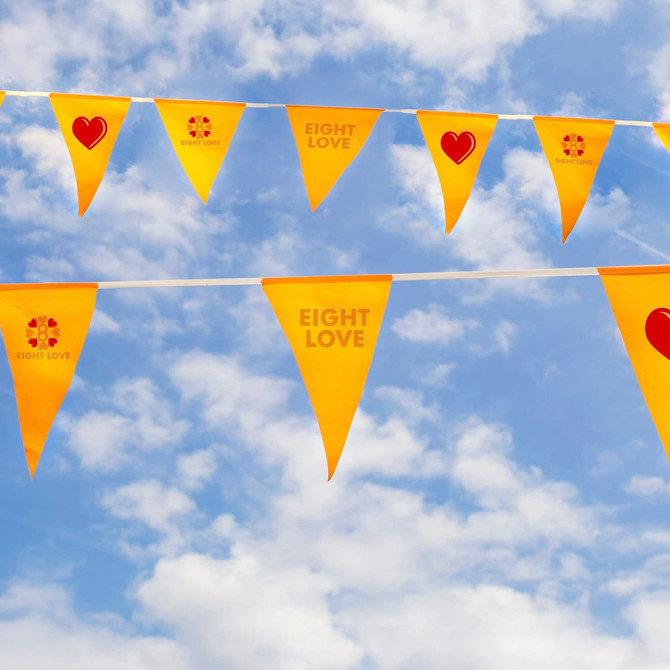 Custom PVC pennant string flags in vibrant yellow with printed designs against a blue sky and fluffy clouds.