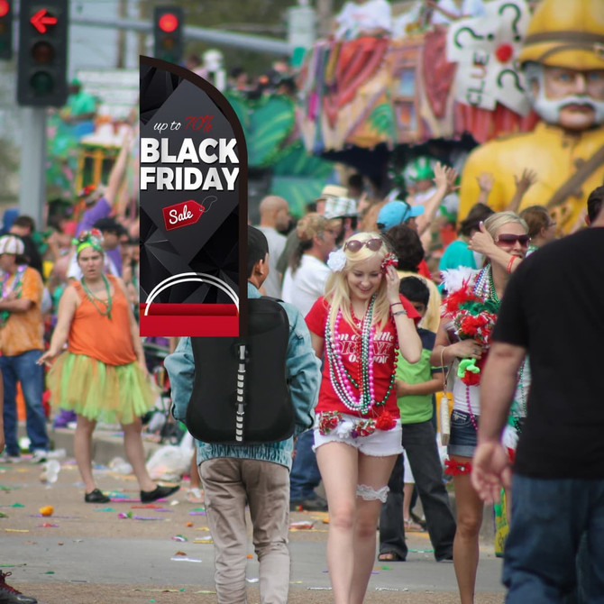 A feather backpack flag features a black and red design, standing amidst a lively festival scene with people celebrating.