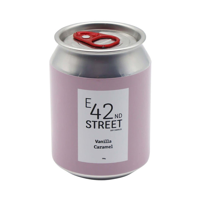 A pink can-shaped candle with a silver lid, featuring a label for 'Vanilla Caramel' fragrance and a logo.