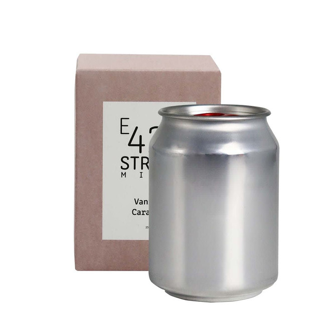 A silver can candle beside a light pink box, featuring a logo on the packaging.