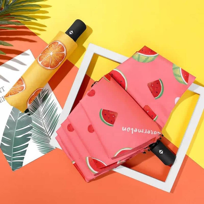 A pink umbrella with watermelon patterns and a black handle, set against a bright yellow and orange background.