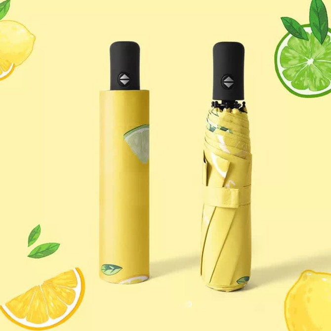 A yellow umbrella with lemon and lime designs, featuring a black handle and a compact storage sleeve.