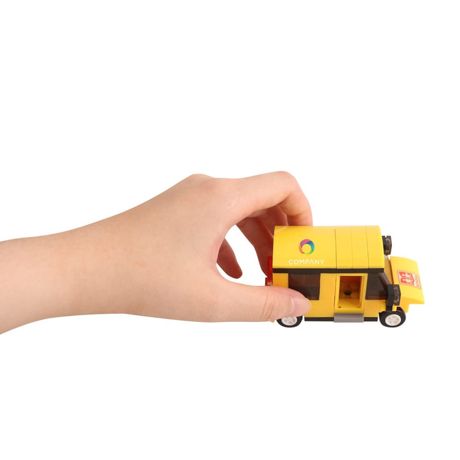 A hand holds a yellow toy delivery truck made of building blocks with a logo on the side.
