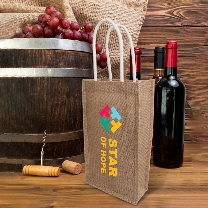 A jute double wine carrier in natural brown, featuring a logo, next to wine bottles and a wooden barrel.