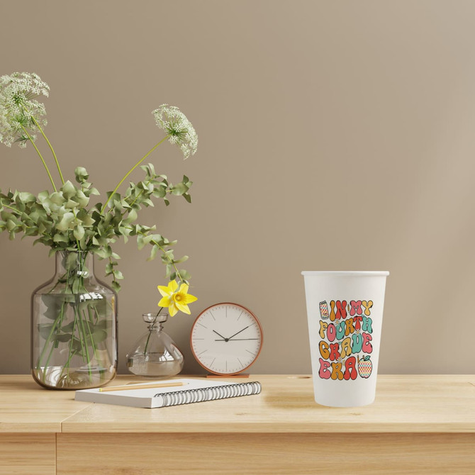 Custom disposable single wall paper cup featuring a colourful design, set on a wooden surface with a clock and plants.