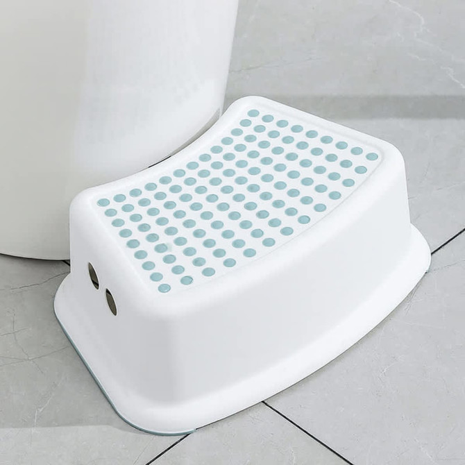 A white step stool with a textured surface and blue dots, placed on tiled flooring. It features ventilation holes.