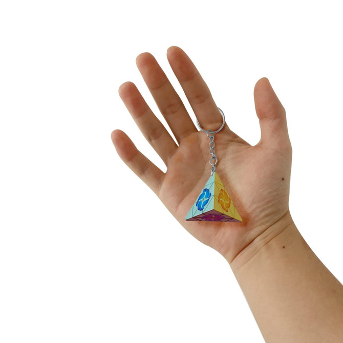 A hand holds a multicoloured puzzle pyramid keyring, featuring a shiny, geometric design.