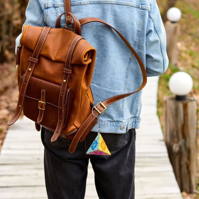 A colourful pyramid-shaped puzzle attached to a brown leather backpack, hanging from a keyring.