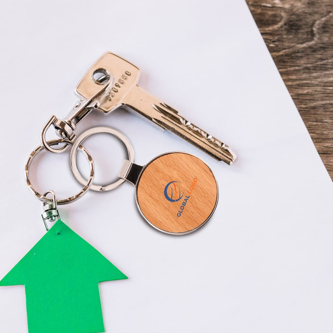 A round wooden keyring with a logo, attached to metal keys and a green arrow tag, on a white surface.