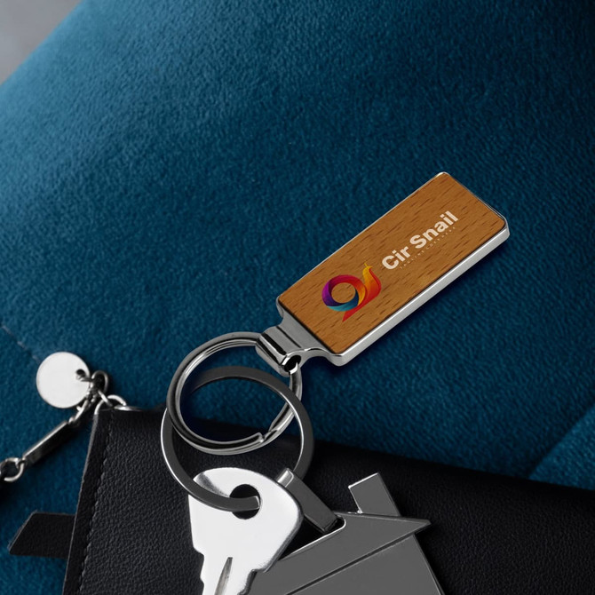 A wooden rectangle keyring featuring a metal keyring attachment and a logo, resting on dark fabric with keys.