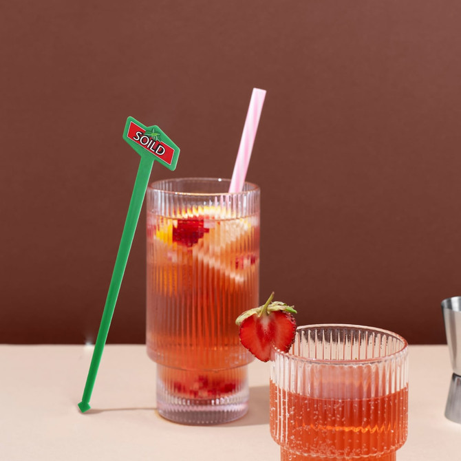 A drink bottle with a green cocktail stirrer, pink straw, and two glasses filled with a fruity drink and strawberries.