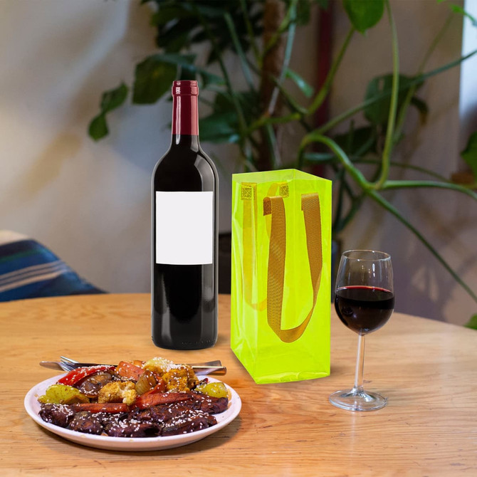A clear jelly wine ice bag in vibrant yellow beside a bottle of red wine and a glass of red wine on a wooden table.
