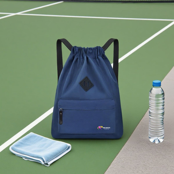 A navy blue drawstring backpack with a front pocket, next to a drink bottle and a towel on a green surface.