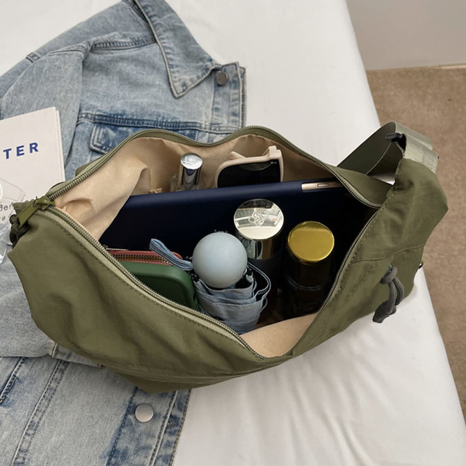 An olive green crossbody bag opened to display various items, including a drink bottle, a notebook, and makeup products.