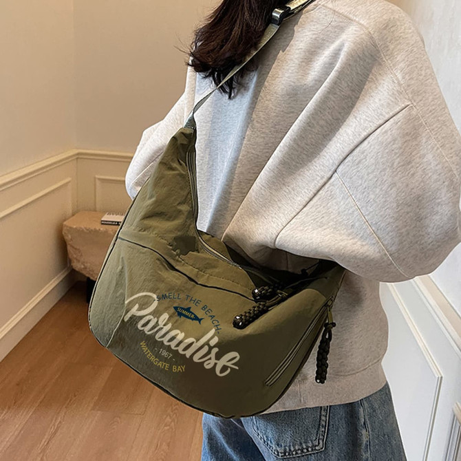 A Dumpling Crossbody Bag in olive green with a logo, worn over a grey sweatshirt, against a light background.