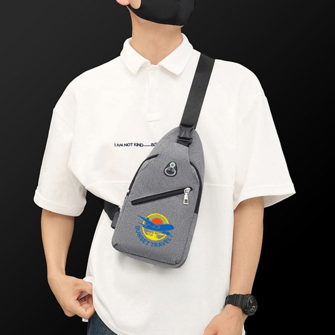 A grey sling chest bag with zippers and a logo, worn across a person's body over a white shirt.
