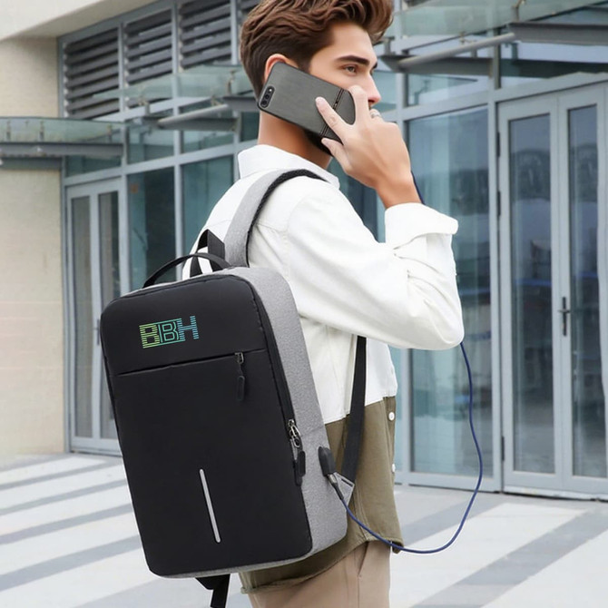 A grey and black laptop backpack with USB charging feature, worn by a person on the phone.