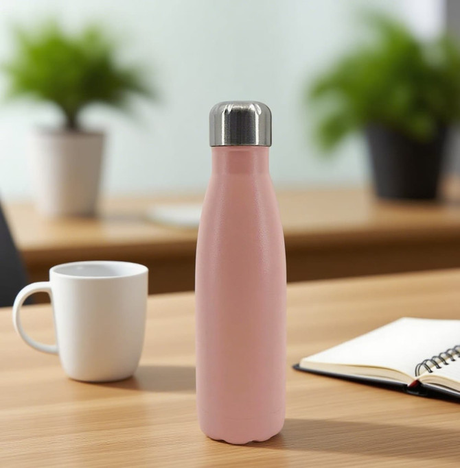A drink bottle in pink with a stainless steel lid, set on a wooden table near a mug and a notebook.