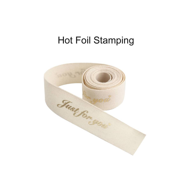 A rolled cotton ribbon in cream featuring gold hot stamping text. It has an elegant and soft appearance.