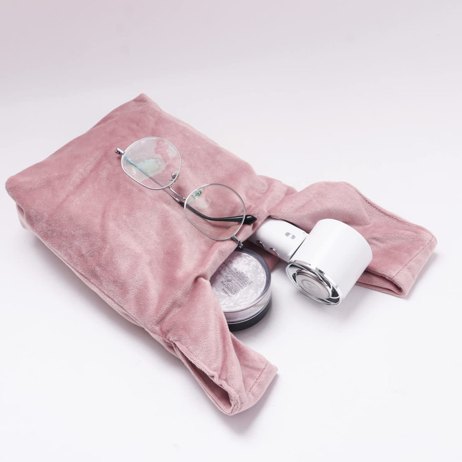 A pink velvet wrist bag containing glasses and a small round container. It has a soft, textured surface.