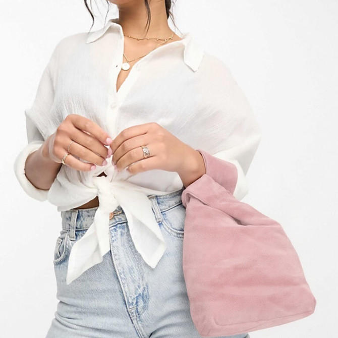 A pink velvet wrist bag is held by a person wearing a white blouse and light blue jeans.