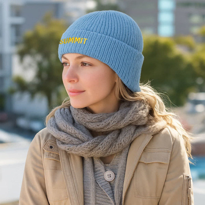 A light blue earflap beanie with a ribbed texture, worn by a woman with a grey scarf, set against an outdoor background.