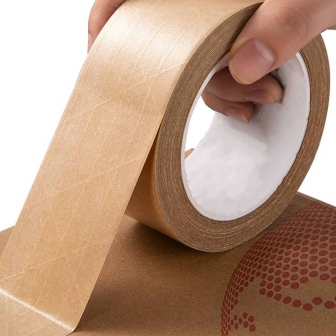A hand holding a roll of self-adhesive reinforced kraft paper tape, featuring a brown colour and diagonal pattern.