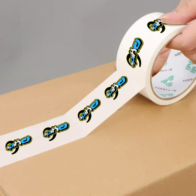 A roll of white packaging tape with a printed logo design, being applied to a cardboard box.