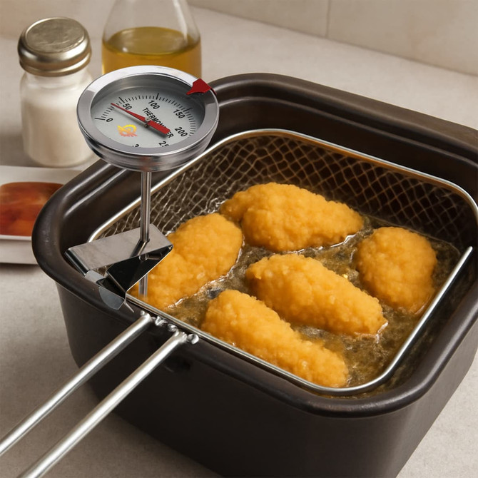 A stainless steel deep fry thermometer sits above a basket of golden fried food in hot oil.
