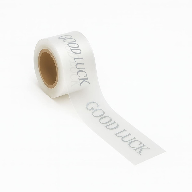 A roll of clear adhesive ribbon with a silver "Good Luck" message printed across it.