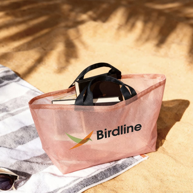 A peach mesh tote bag with black handles, featuring a logo, and holding sunglasses and a book.