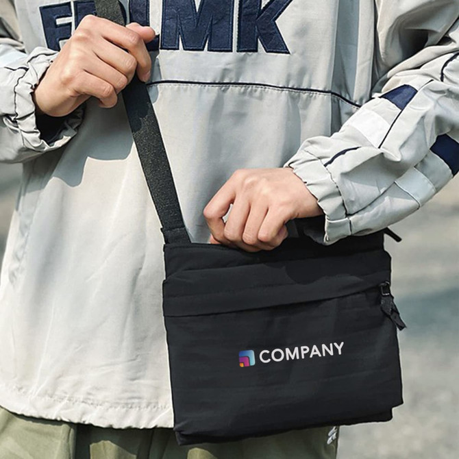 A black lightweight crossbody bag with an adjustable strap and a logo on the front, being held by a person.