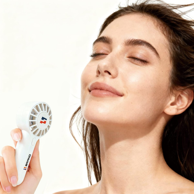 A Mini Travel Handheld Fan in white, held by a person with a serene expression, featuring a logo.